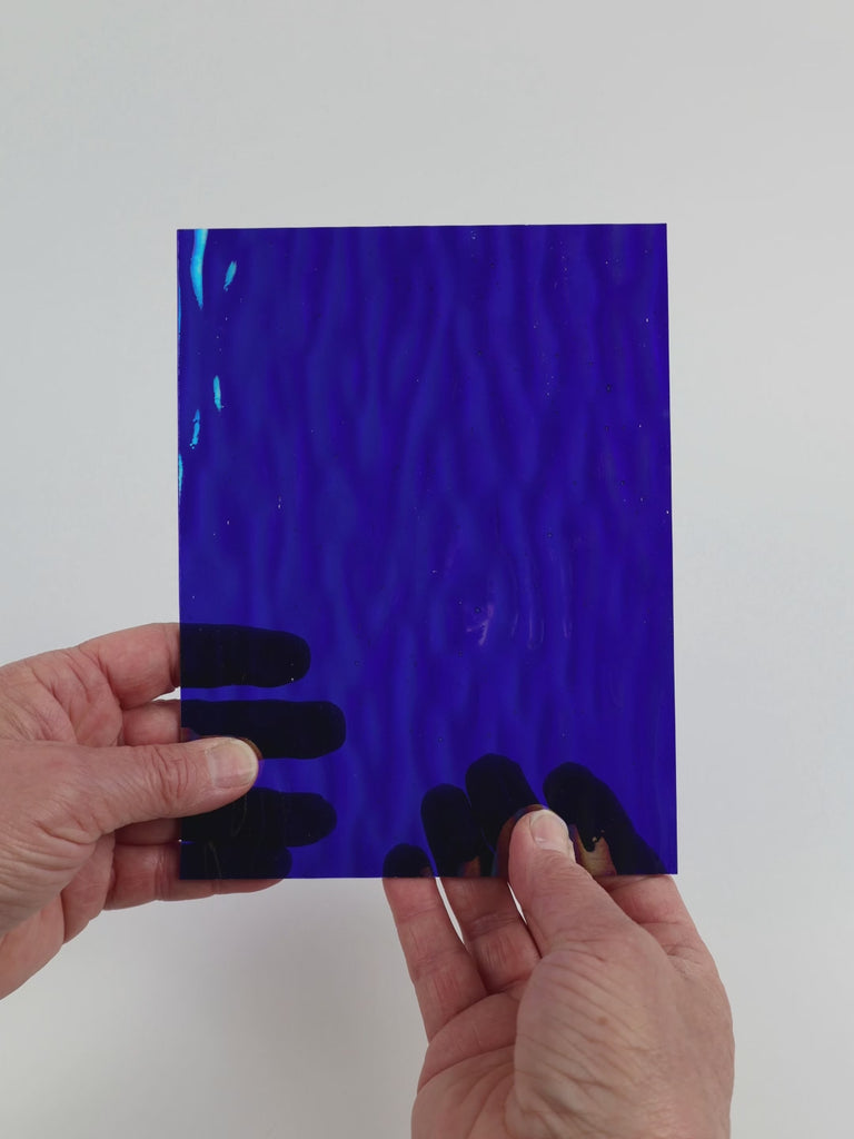 Video of the Mirrored Ink glass plate in iridescent ripple transparent blue, 15x19cm, held up and tilted to show its pattern and transparency
