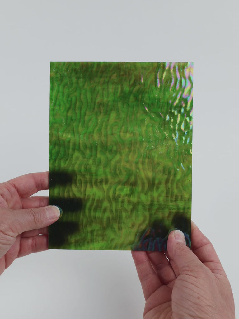 Video of the Camouflage Wavy iridescent glass plate in iridised ripple translucent green, 15x19cm, held up and tilted to show its pattern and transparency