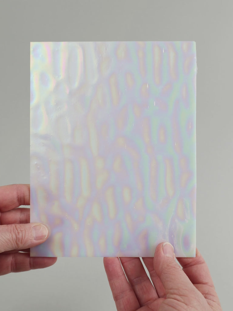 Video of the white pearlescent glass plate in white translucent iridescent, 15x19cm, held up and tilted to show its pattern and transparency
