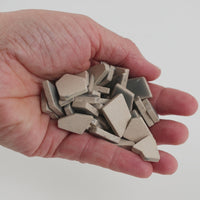 Video of Flip ceramic puzzle pieces in smoke grey, opaque glazed porcelain, 4–20 mm, held in a hand and poured out to show their shapes and finish
