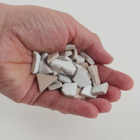 Video of Flip ceramic puzzle pieces in white, opaque glazed porcelain, 4–20 mm, held in a hand and poured out to show their shapes and finish