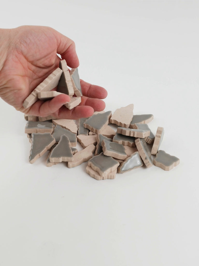 Video of Flip XL ceramic puzzle pieces in smoke grey, opaque glazed porcelain, 20–60 mm, picked up from a pile by hand and dropped back to show their size, shapes and finish