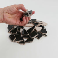 Video of Flip XL ceramic puzzle pieces in anthracite, opaque glazed porcelain, 20–60 mm, picked up from a pile by hand and dropped back to show their size, shapes and finish