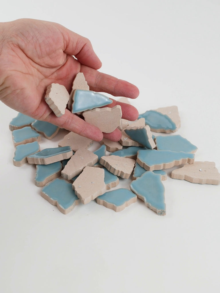 Video of Flip XL ceramic puzzle pieces in ice blue, opaque glazed porcelain, 20–60 mm, picked up from a pile by hand and dropped back to show their size, shapes and finish