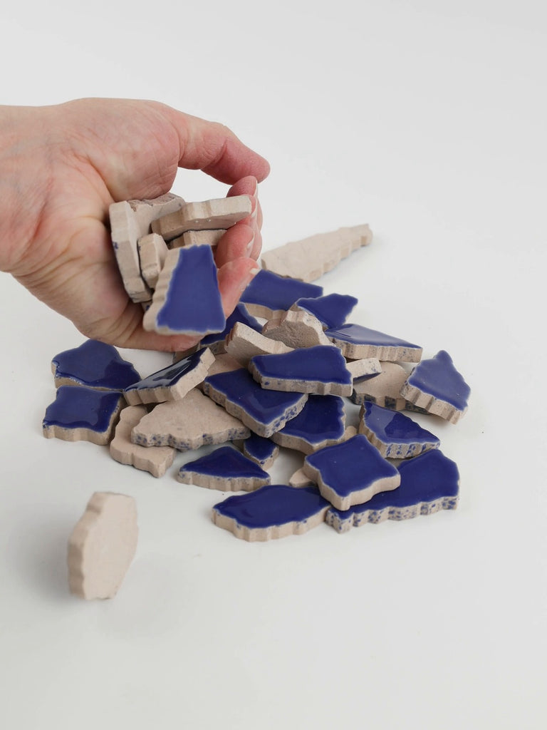 Video of Flip XL ceramic puzzle pieces in cobalt, opaque glazed porcelain, 20–60 mm, picked up from a pile by hand and dropped back to show their size, shapes and finish