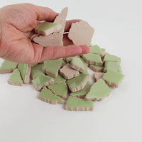 Video of Flip XL ceramic puzzle pieces in linden green, opaque glazed porcelain, 20–60 mm, picked up from a pile by hand and dropped back to show their size, shapes and finish