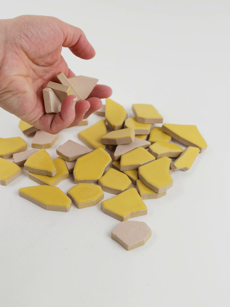 Video of Flip XL ceramic puzzle pieces in corn, opaque glazed porcelain, 20–60 mm, picked up from a pile by hand and dropped back to show their size, shapes and finish
