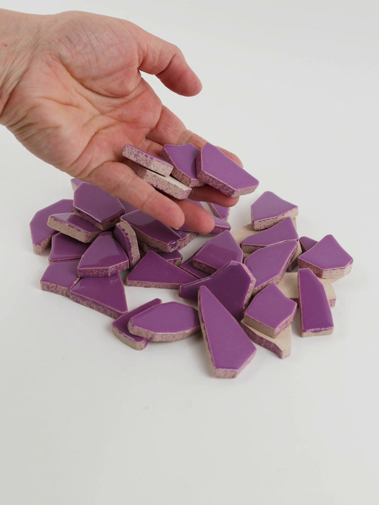 Video of Flip XL ceramic puzzle pieces in purple, opaque glazed porcelain, 20–60 mm, picked up from a pile by hand and dropped back to show their size, shapes and finish