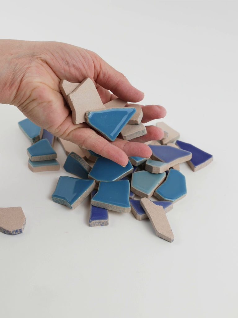 Video of Flip XL ceramic puzzle pieces in blue mix, opaque glazed porcelain, 20–60 mm, picked up from a pile by hand and dropped back to show their size, shapes and finish
